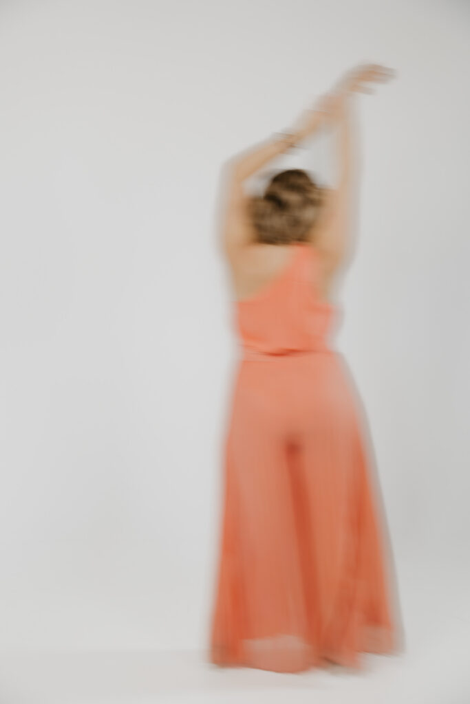 Motion shot of a transformational coach with arms raised overhead, orange dress in blurred movement