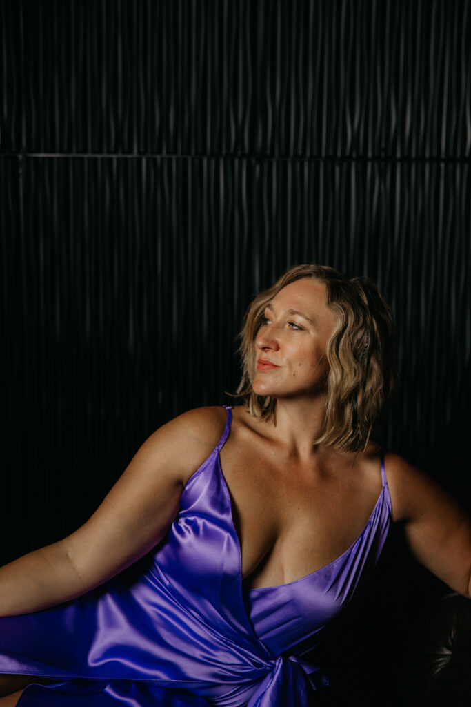 Woman seated looking upward in a purple satin dress, moody low lighting