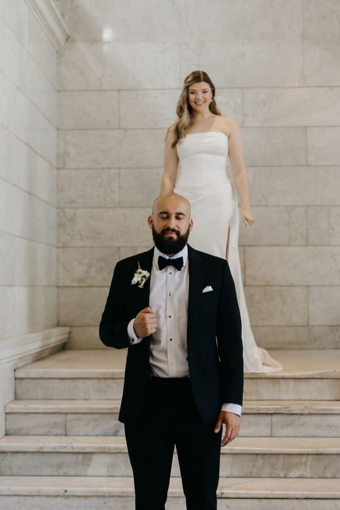 Bride stands above her groom on a marble staircase as he looks up at her