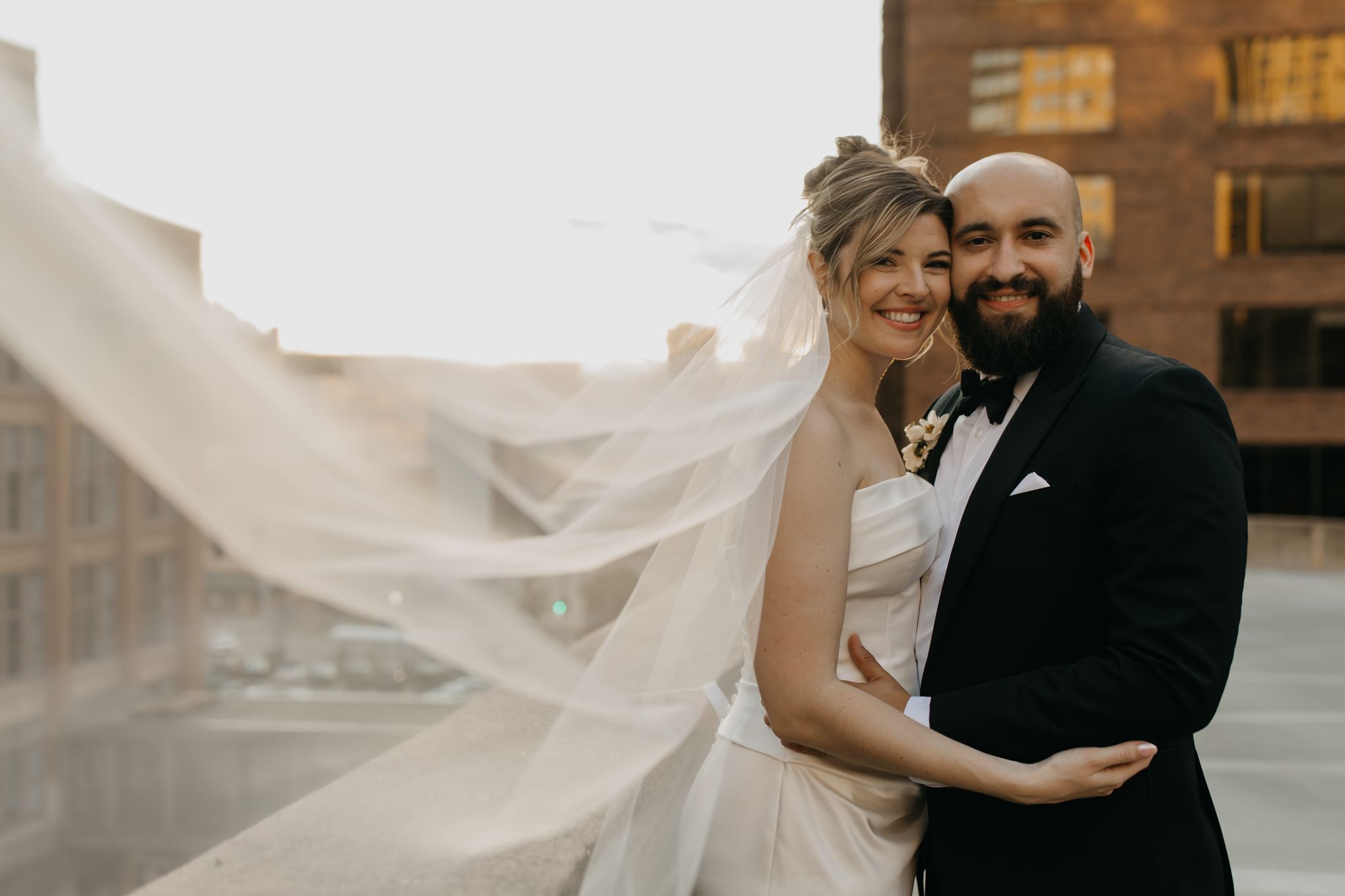 Bride and groom embrace on a rooftop with veil blowing in the wind near their downtown Minneapolis wedding venue