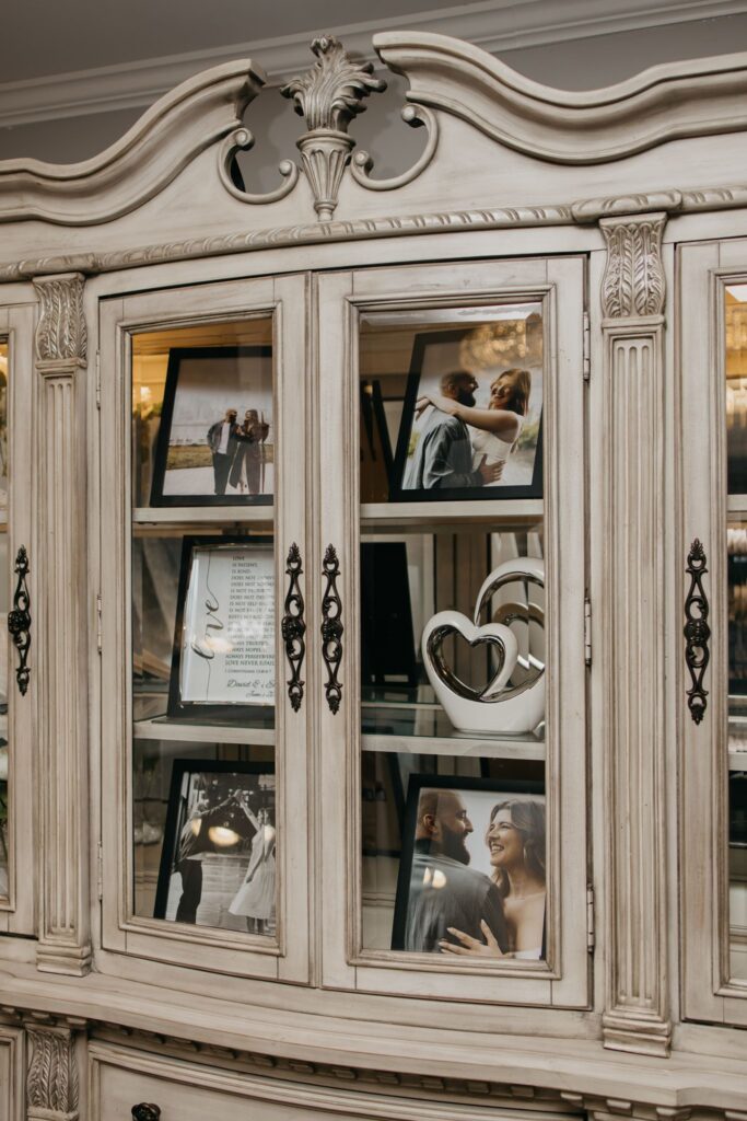 Vintage china cabinet displaying framed photos of the couple at the reception