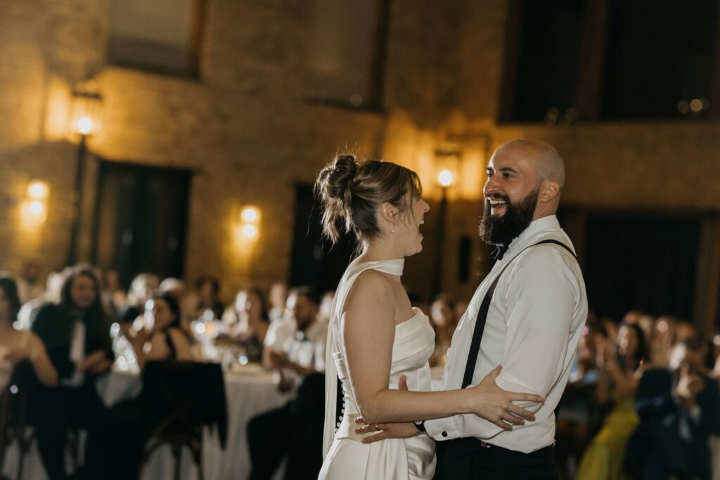 Bride laughing closely with a wedding party member in warm evening light