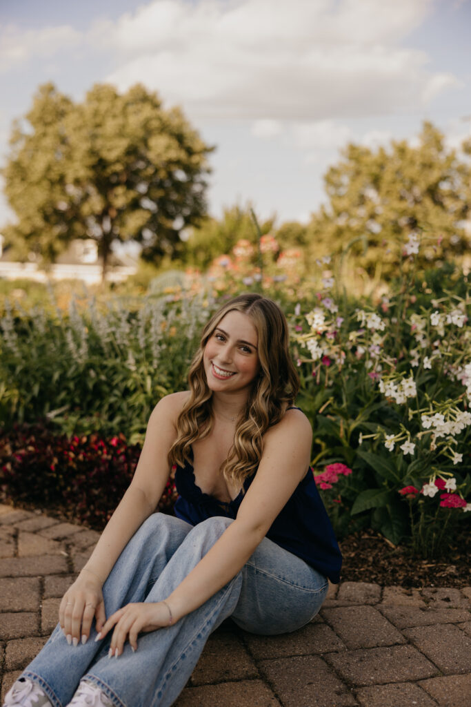 senior girl in navy top sitting on brick garden path in jeans