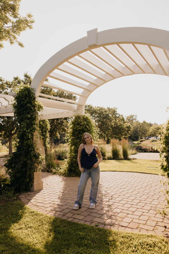 senior girl in navy top and jeans walking under pergola archway
