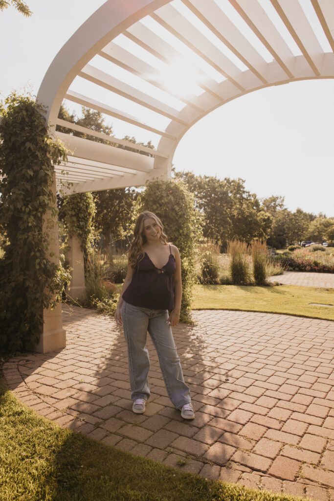 senior girl in navy top and jeans standing under garden pergola