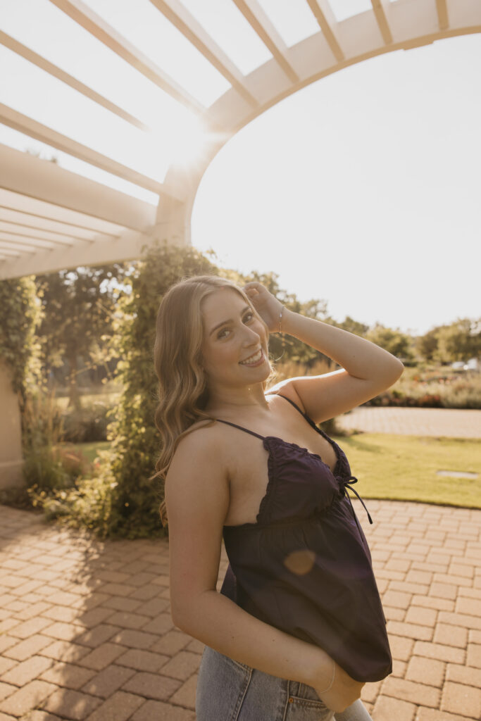 senior girl in navy top close-up portrait, backlit by sun under pergola