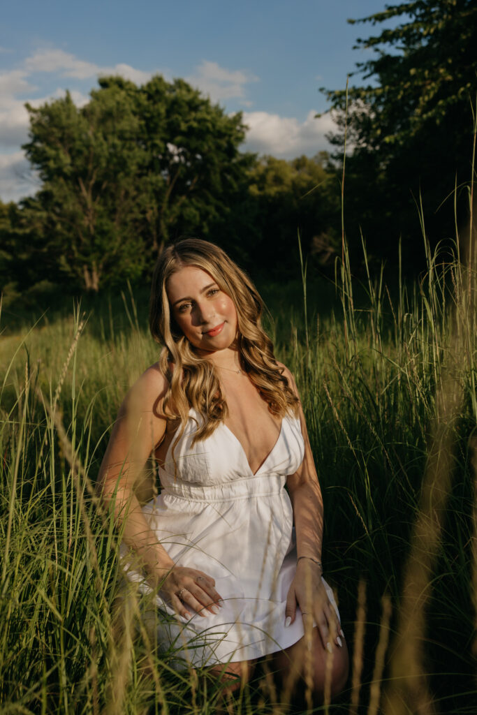 senior girl in white dress standing in tall grass field, hand at hip, nature-inspired senior photos