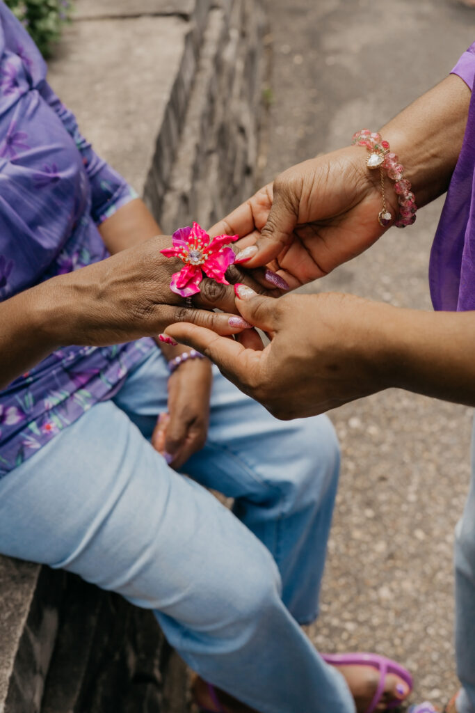 Close-up of daughter placing a pink flower ring on her mother's hand, matching purple sleeves visible