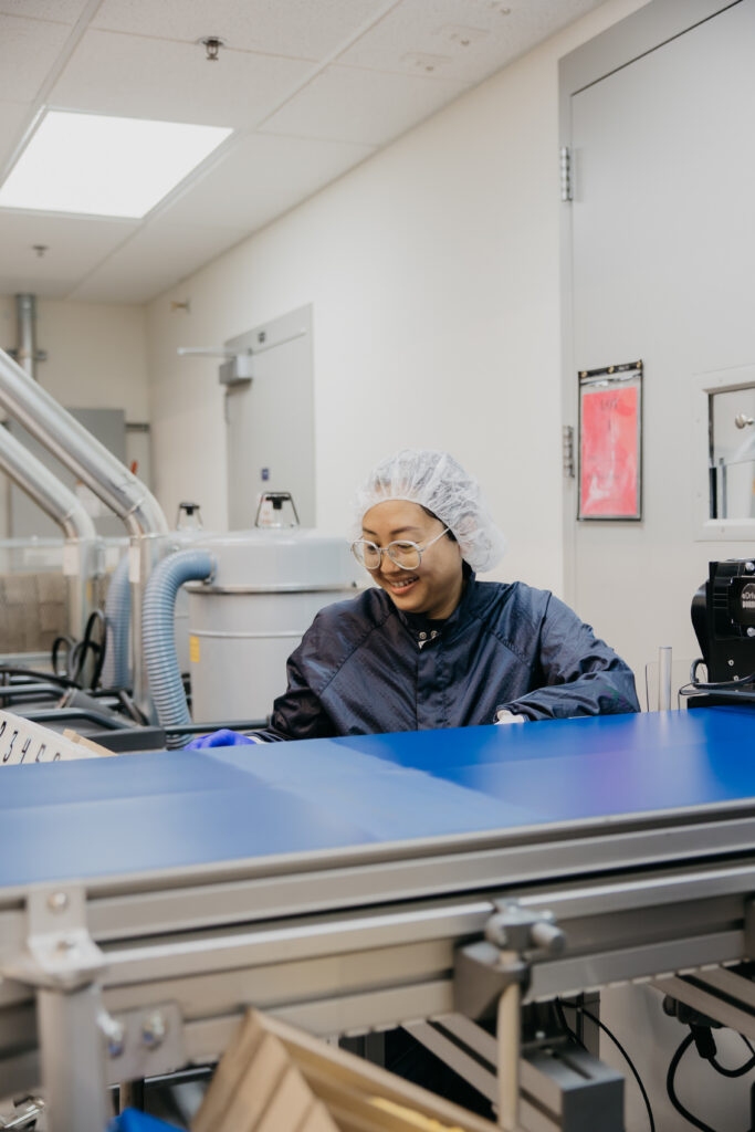 Employee seated at packaging line equipment, smiling toward the camera