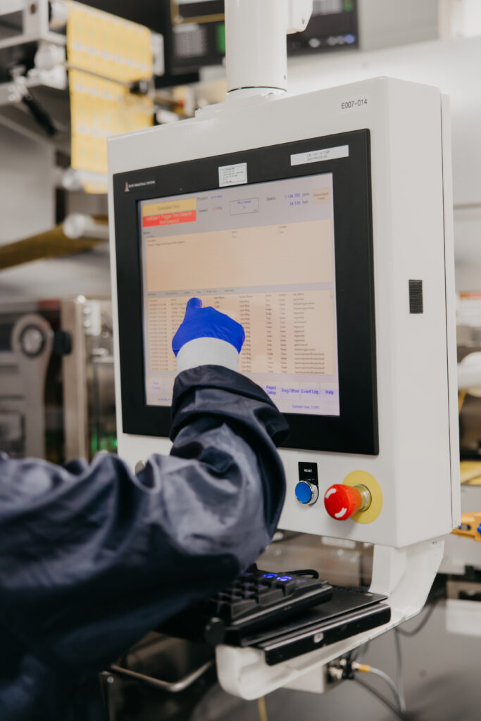 Gloved hand adjusting a digital control panel on pharmaceutical manufacturing equipment