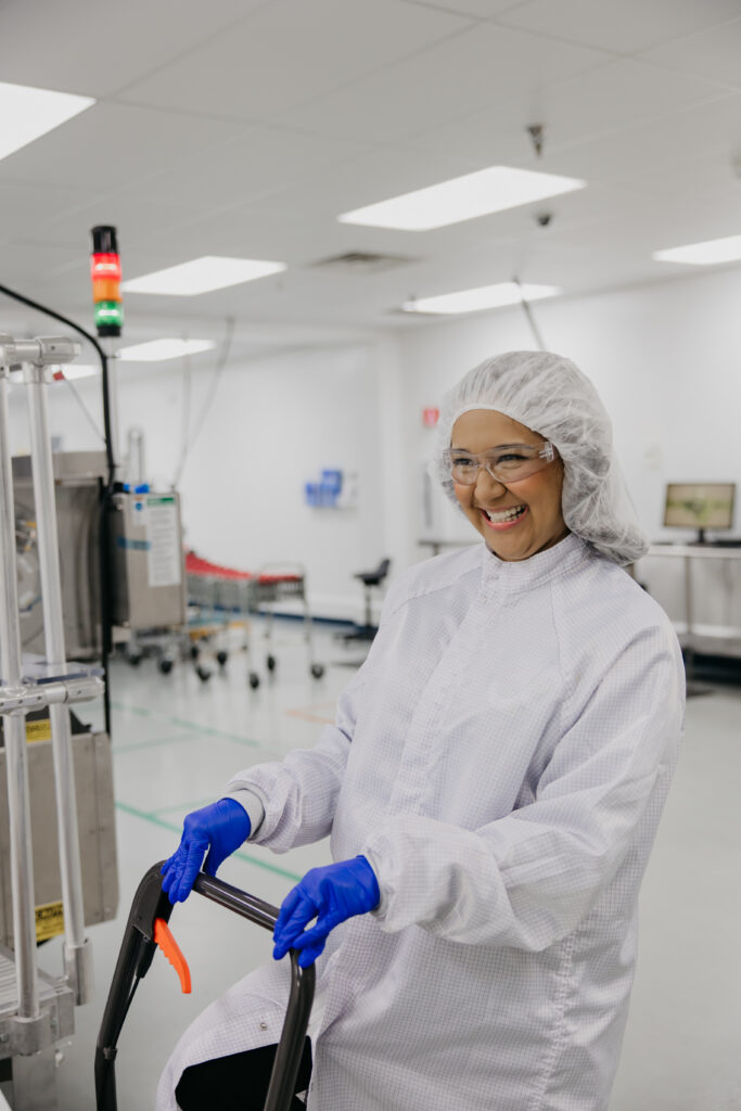 Smiling technician in white cleanroom coveralls and hairnet pushing equipment cart on the LTS Lohmann St. Paul production floor