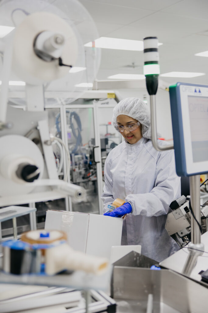 Technician in white gown operating a labeling machine on the packaging line