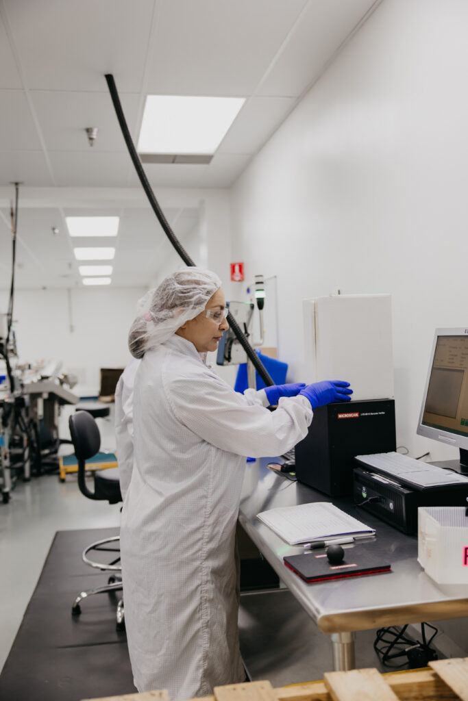 Technician in white coveralls and blue gloves operating equipment at a computer workstation