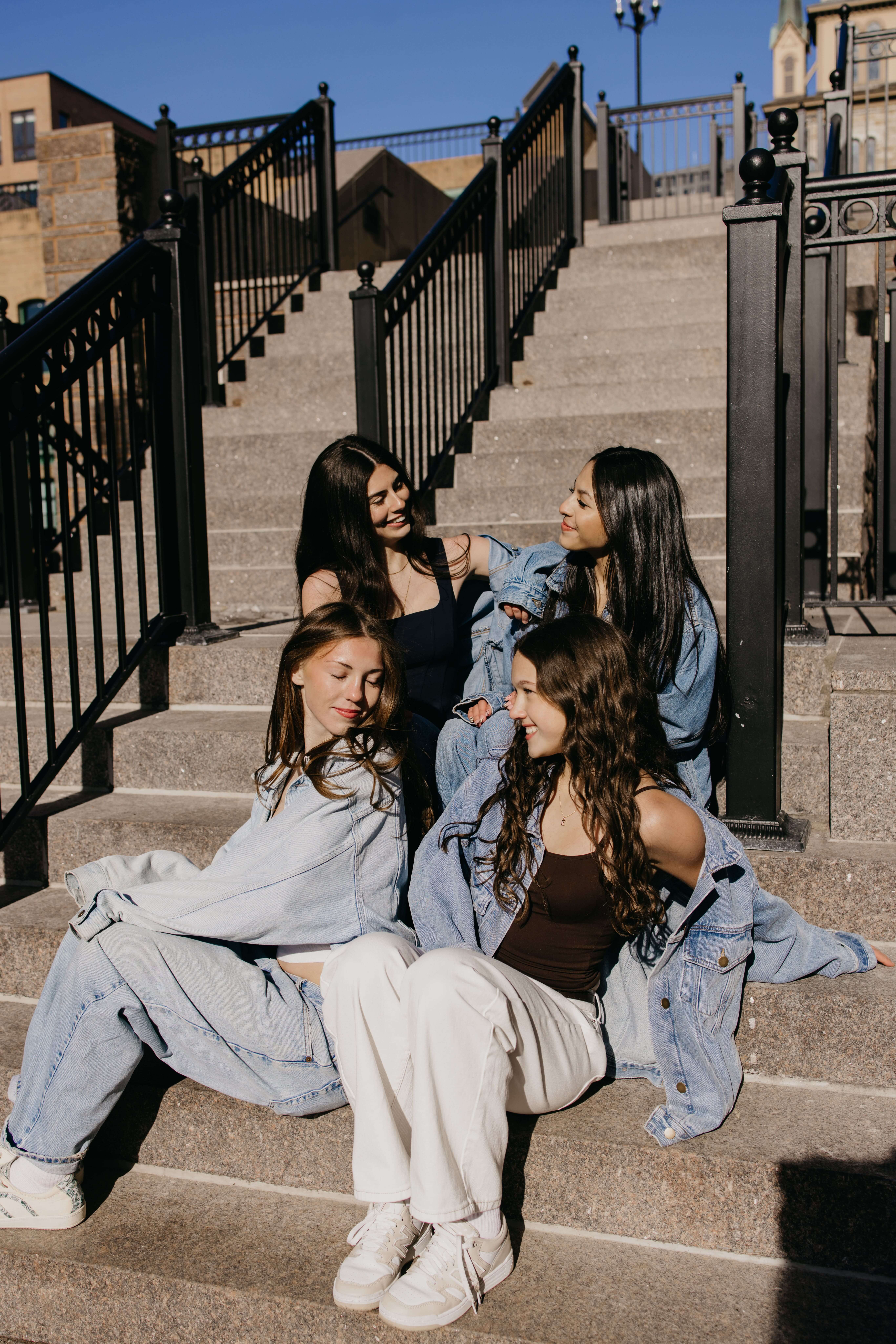 Lucy and three friends in denim jackets sitting and laughing together on a downtown Minneapolis stone staircase during senior pictures with friends