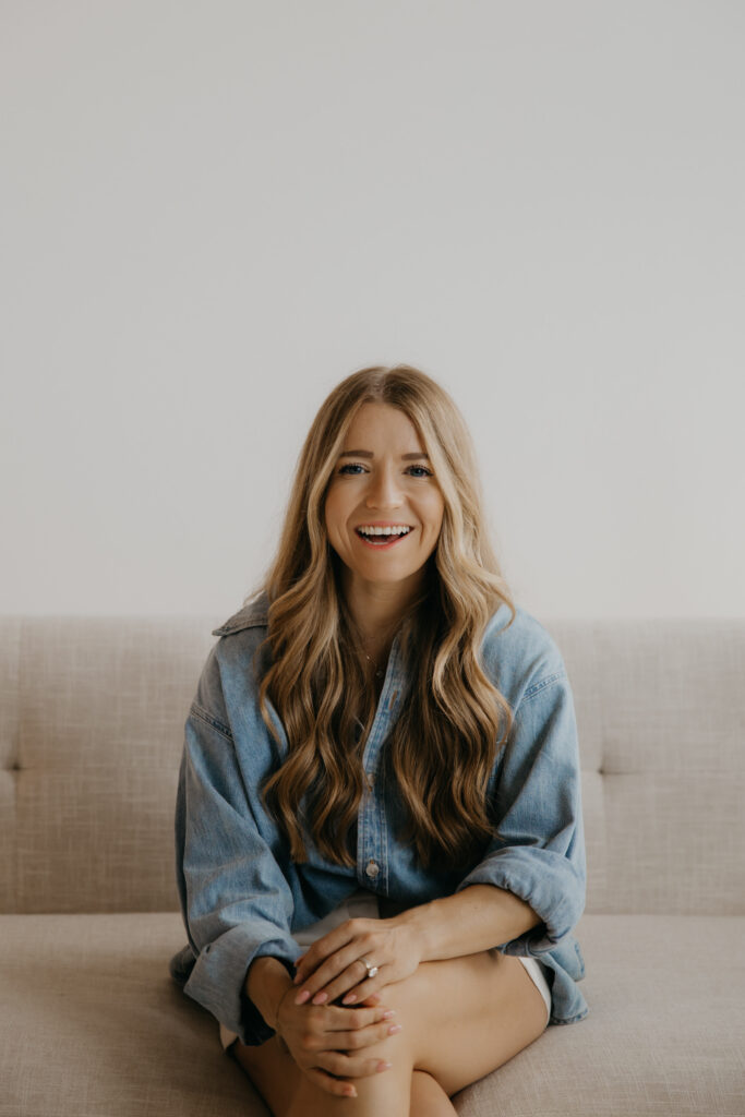 Content creator laughing on couch in oversized denim shirt, hands clasped over knees