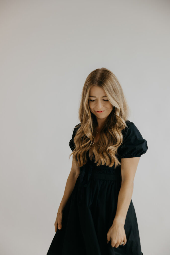 Content creator looking down and smiling in black puff-sleeve dress