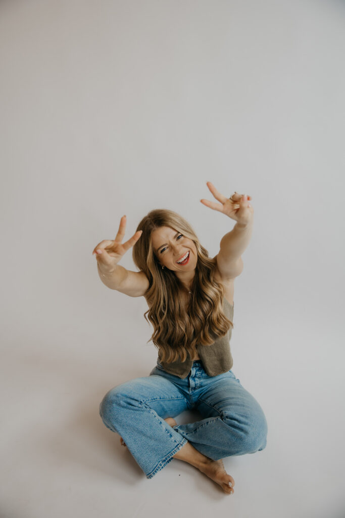 Content creator sitting cross-legged making peace signs in denim shirt and jeans