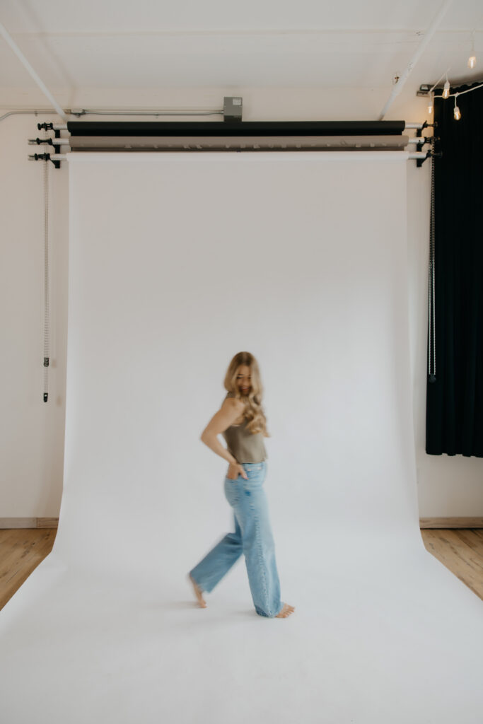 Content creator walking across white studio backdrop in wide-leg jeans