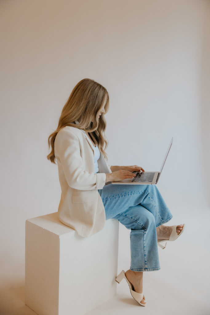 Content creator seated on white block working on laptop, profile view