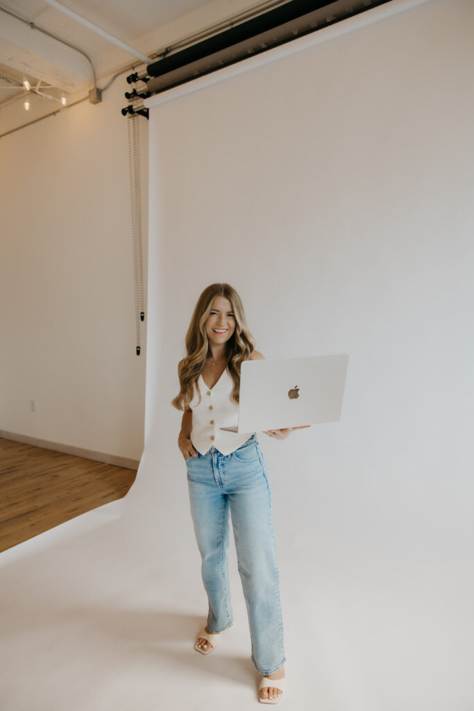 Content creator standing in profile holding laptop in white studio