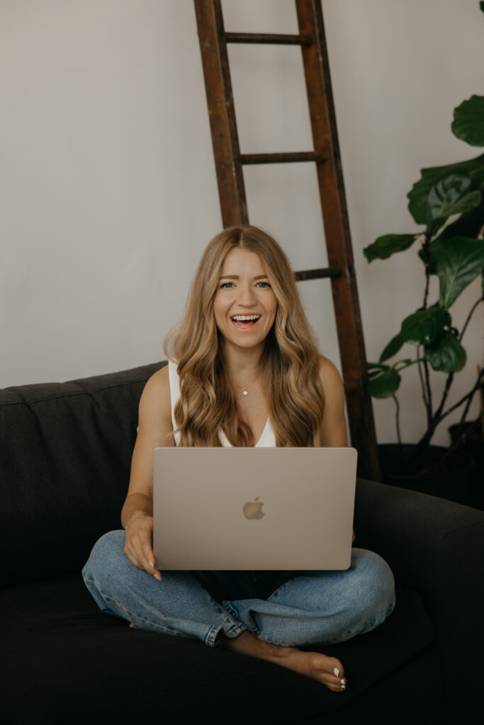 Content creator laughing on couch with laptop, styled with plant and ladder decor