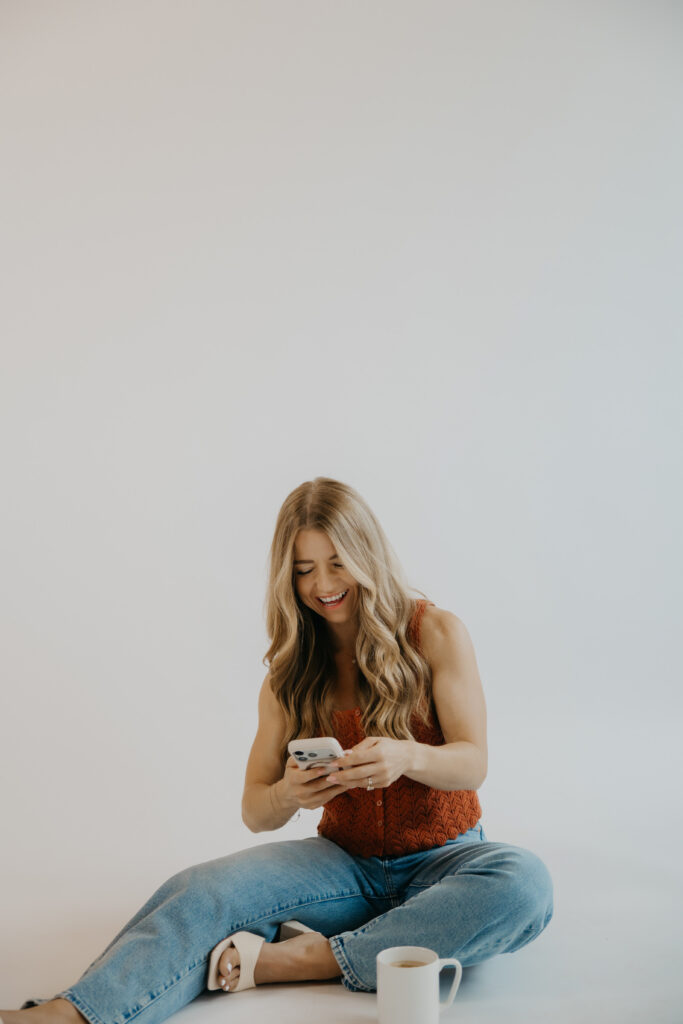Content creator smiling down at phone while seated cross-legged