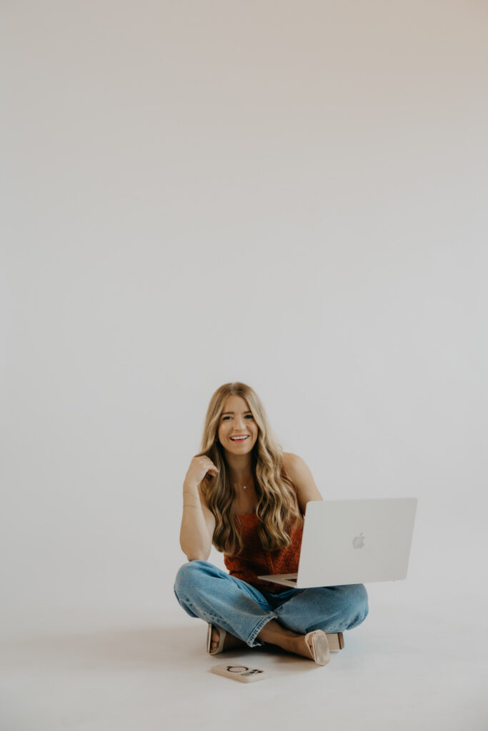 Content creator sitting cross-legged with laptop open, rust top and jeans