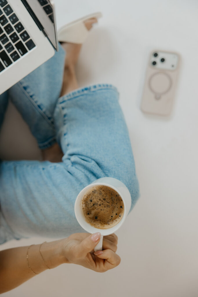 Flatlay of laptop, phone, and coffee mug on denim lap during content creator photoshoot