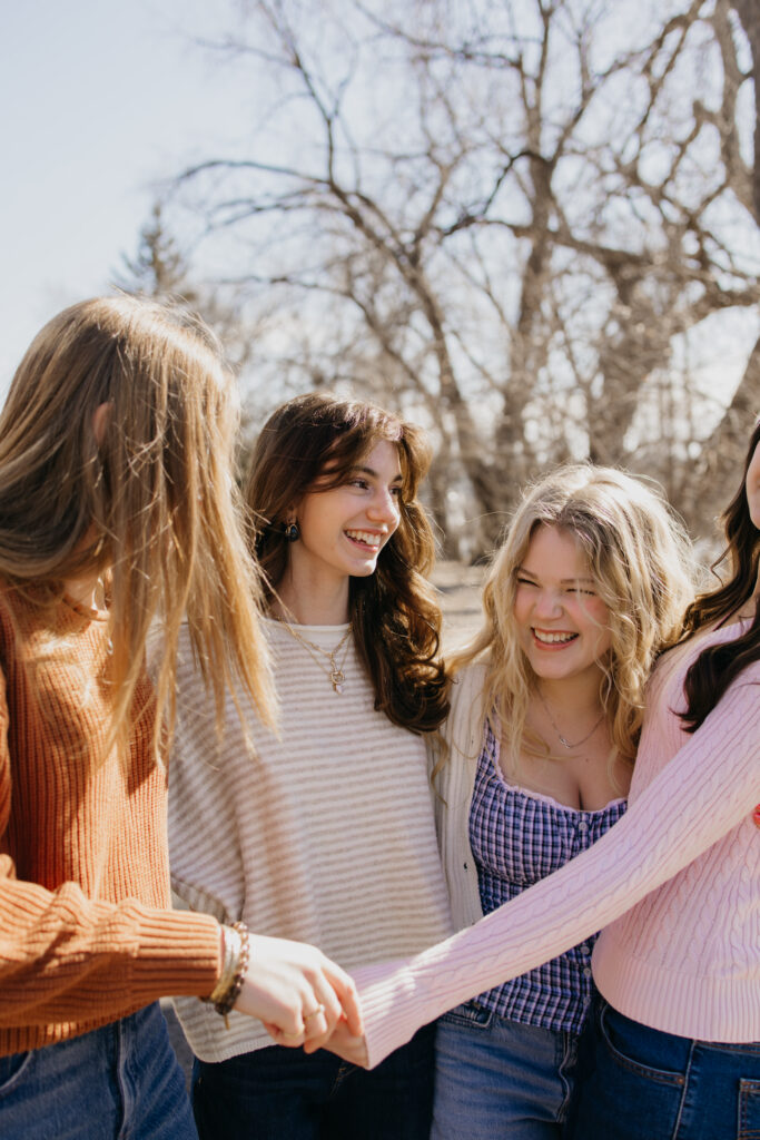 Three senior friends holding hands and smiling closely together on a sunlit brick path