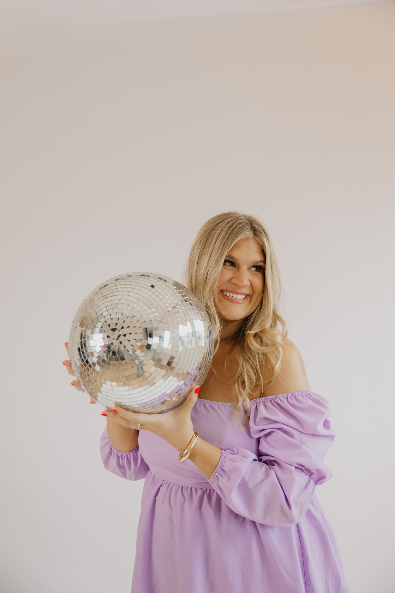 Real estate investing coach in lavender dress holding disco ball during playful brand photography session
