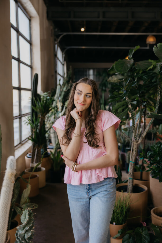 Minneapolis senior in pink top posing among potted cacti during senior photography session with mom
