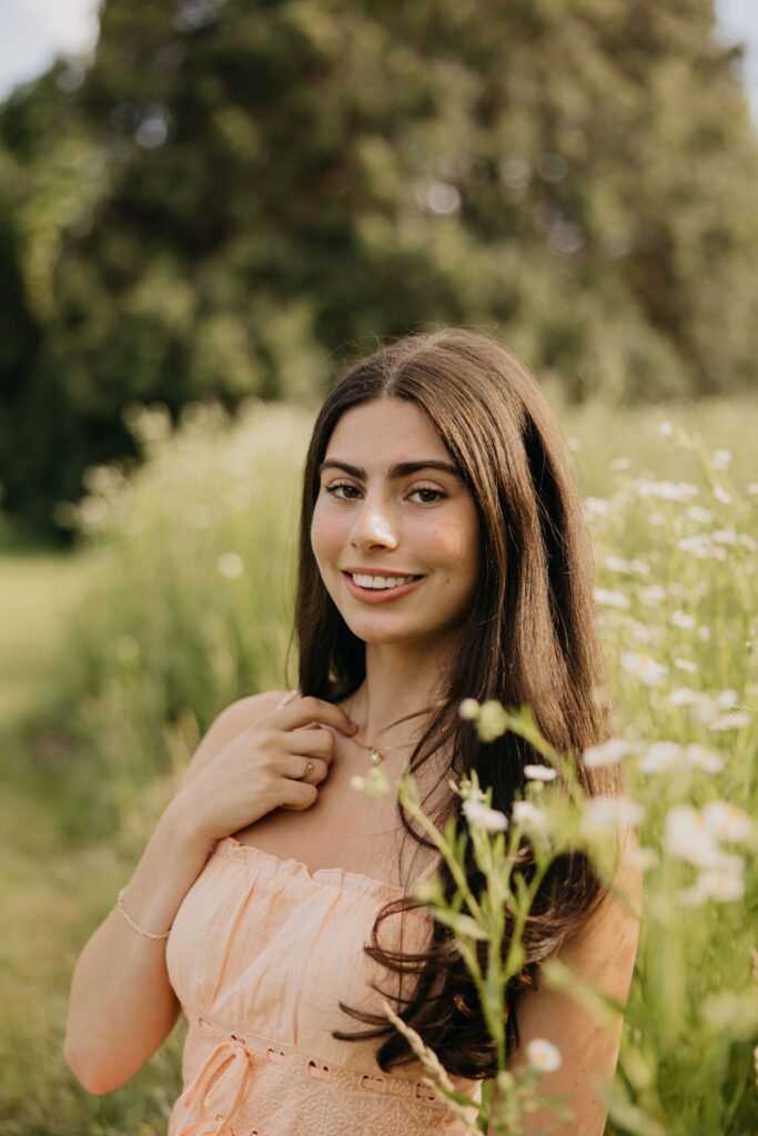 Close-up of senior in peach dress smiling in a wildflower field