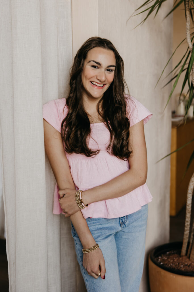 Minneapolis senior in pink top leaning against a curtain, smiling, during senior photography session with mom