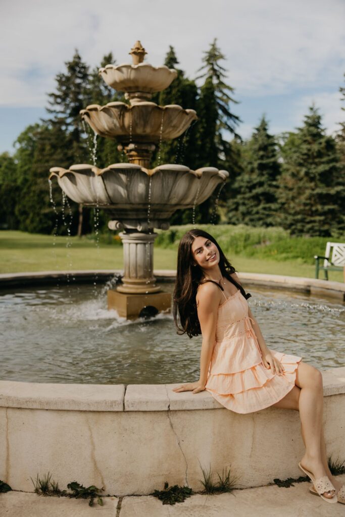 Senior in peach dress in profile sitting on a stone fountain ledge