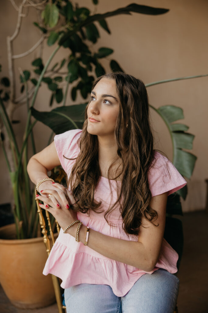 Minneapolis senior in pink top seated in a woven chair during senior photography session with mom