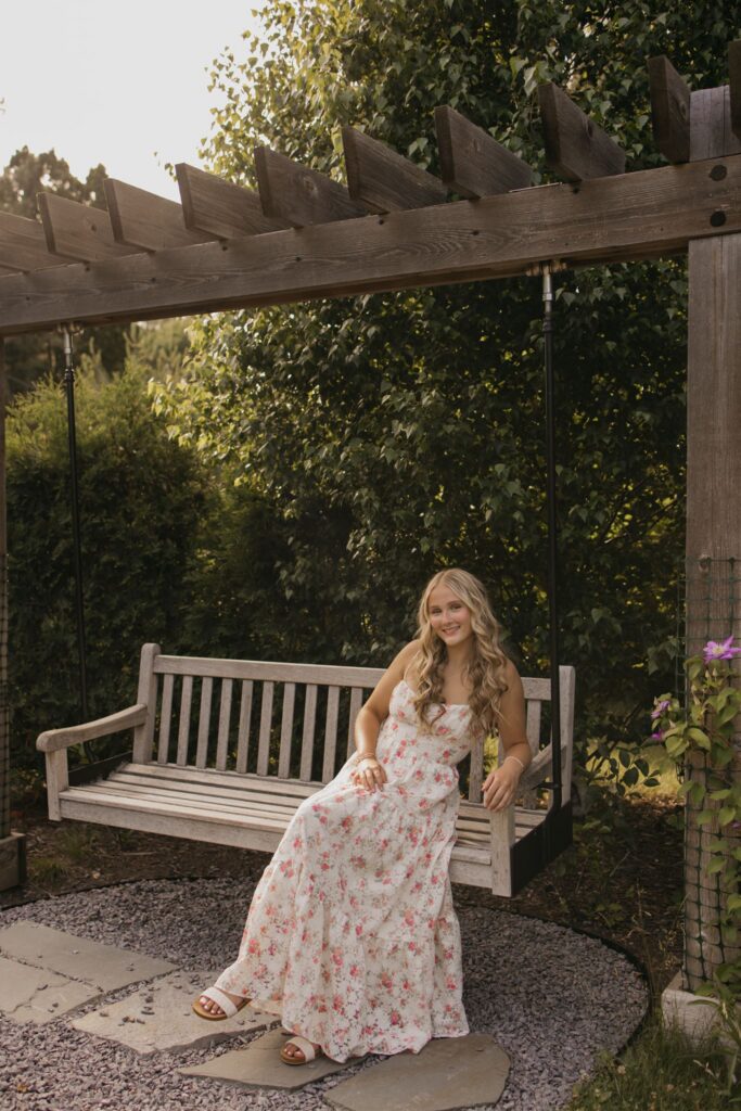 senior girl seated sideways on a garden swing bench, pergola and greenery in the background