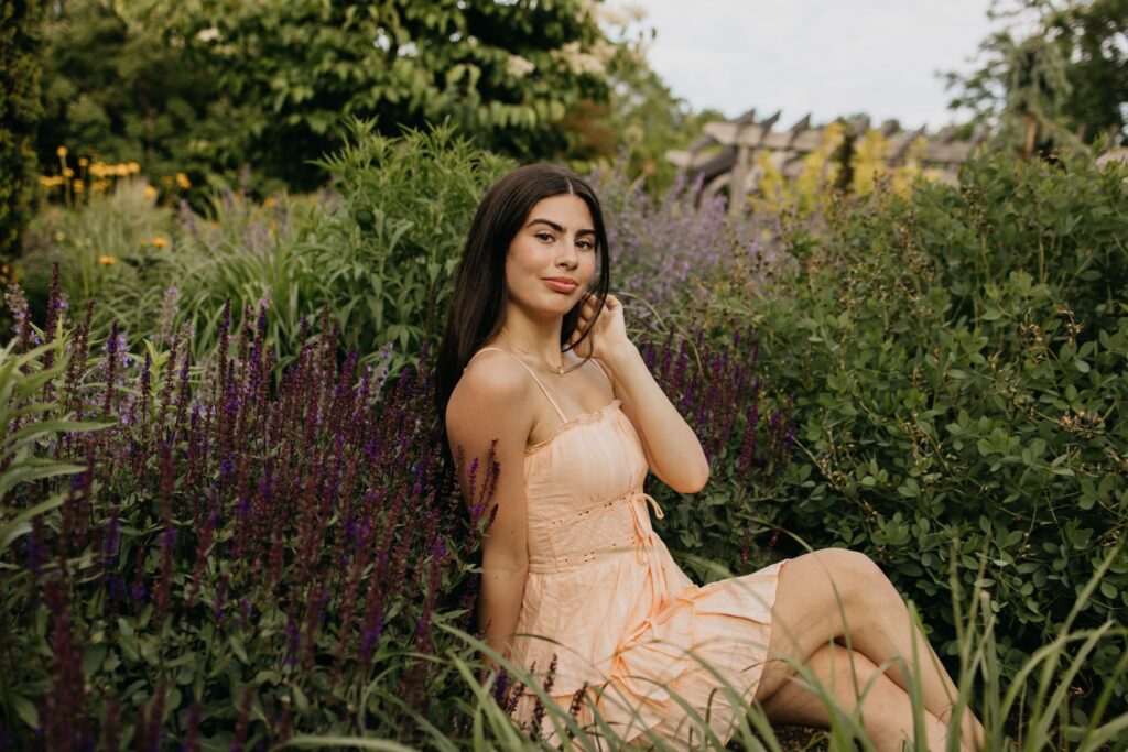 Senior in peach dress sitting among tall purple salvia blooms
