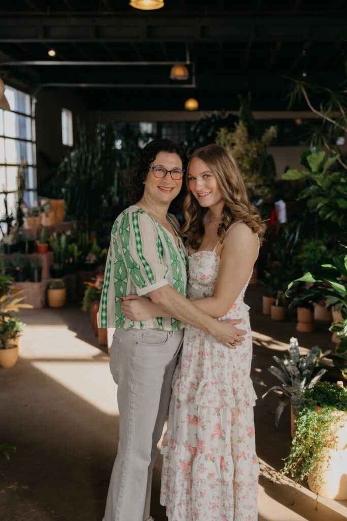 Mom embracing her senior daughter in floral dress, surrounded by greenery, during Minneapolis senior photography session with mom