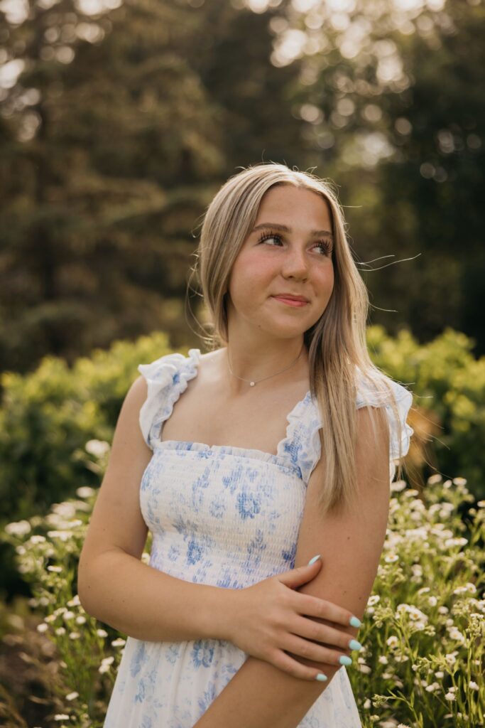 Close-up of blonde senior in blue floral dress smiling in a garden setting