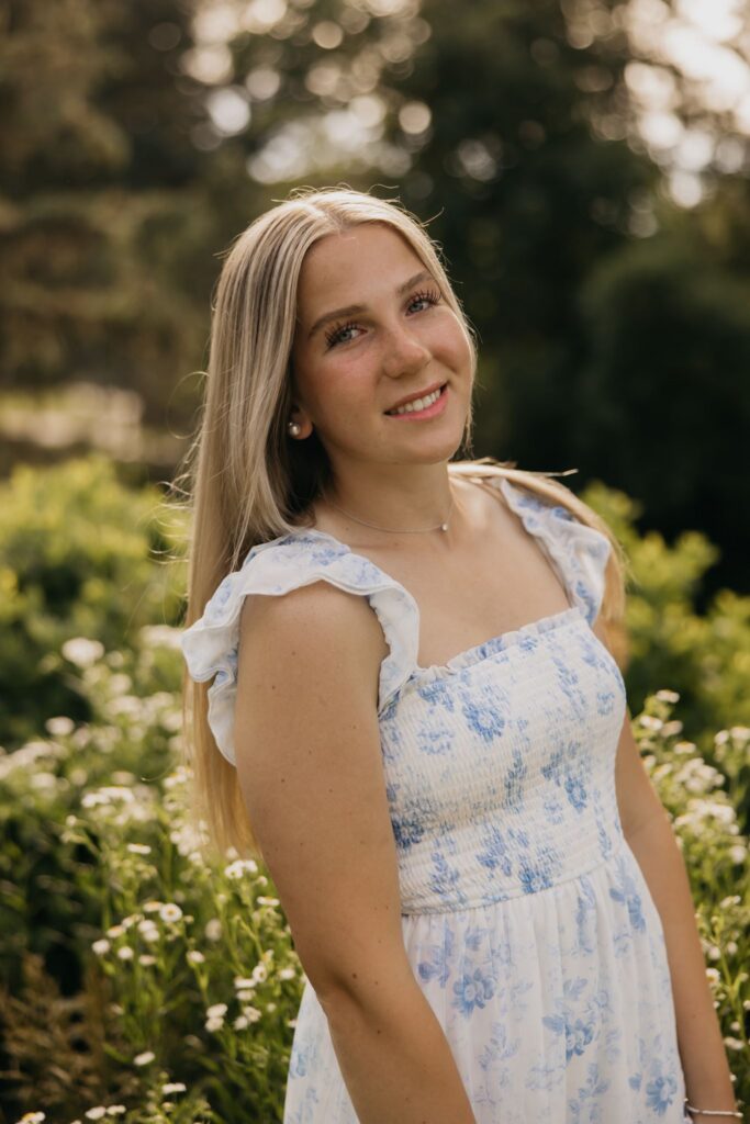 Close-up of blonde senior in blue floral dress smiling in a garden