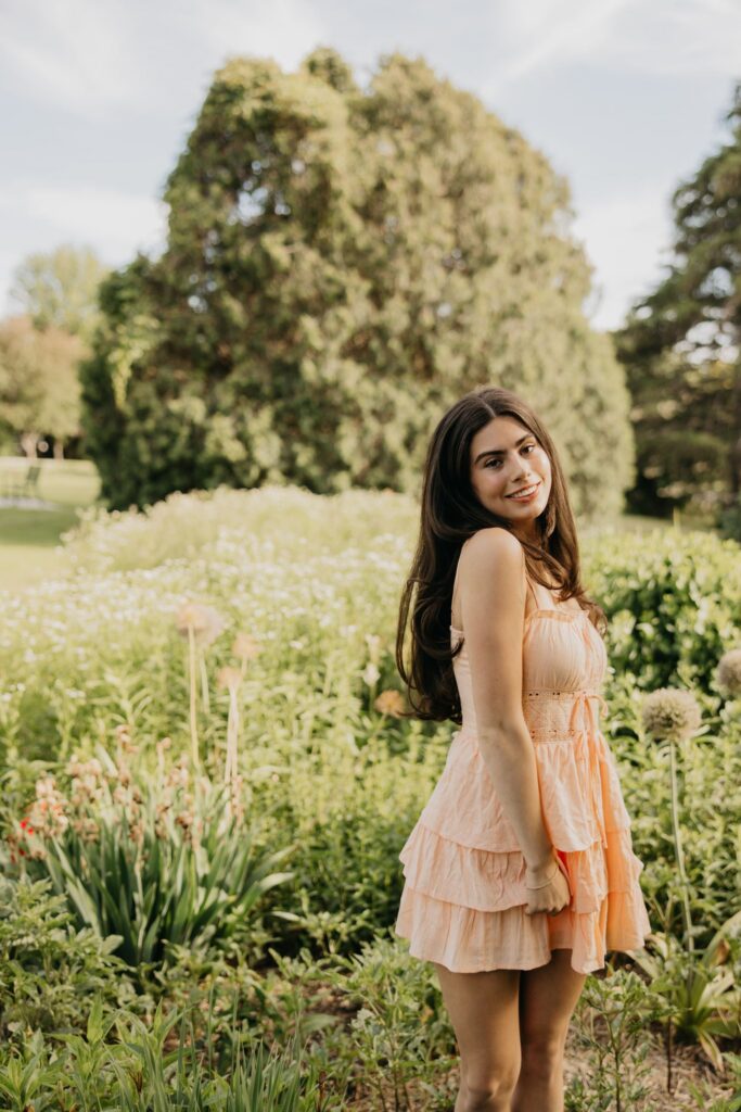 Senior in peach dress standing in a wildflower field during golden hour senior photos