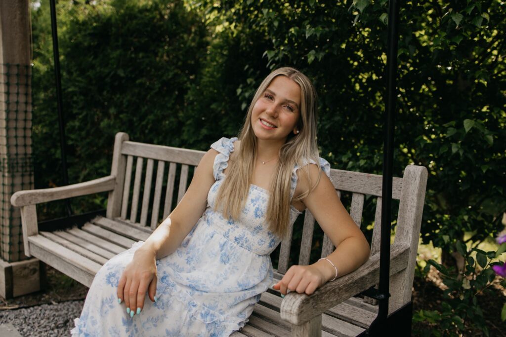 Close-up of blonde senior in blue floral dress smiling on a wooden bench