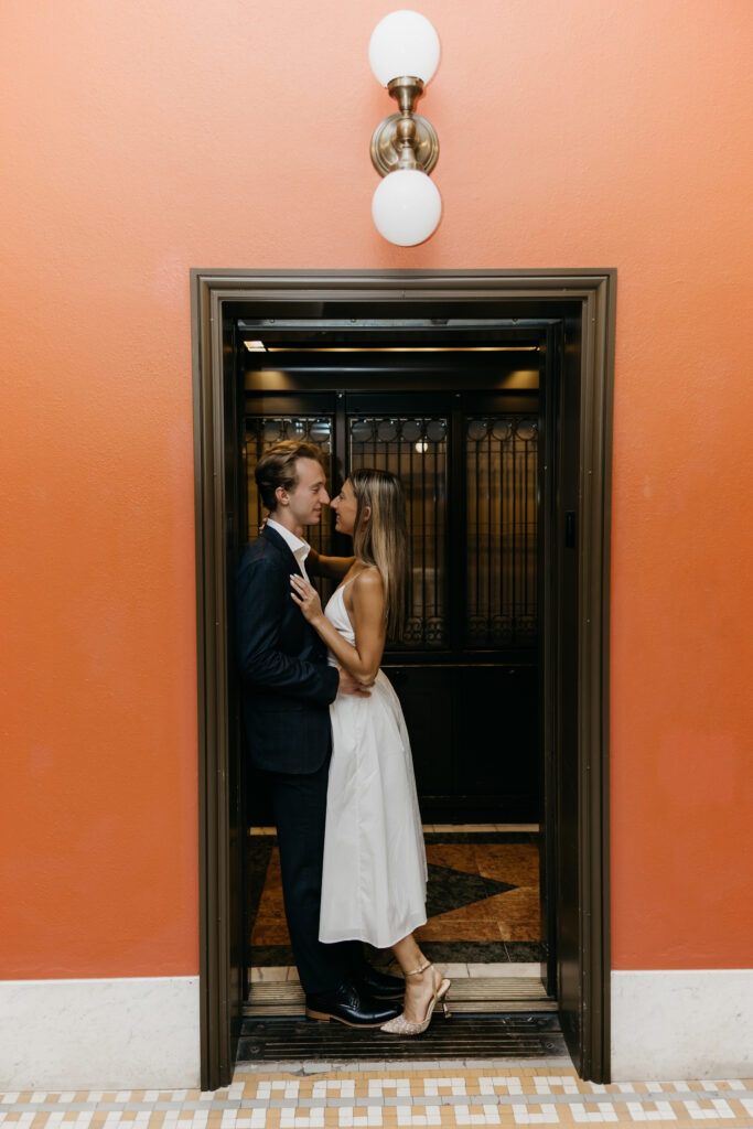 Couple kissing inside a vintage elevator with orange walls and brass sconces