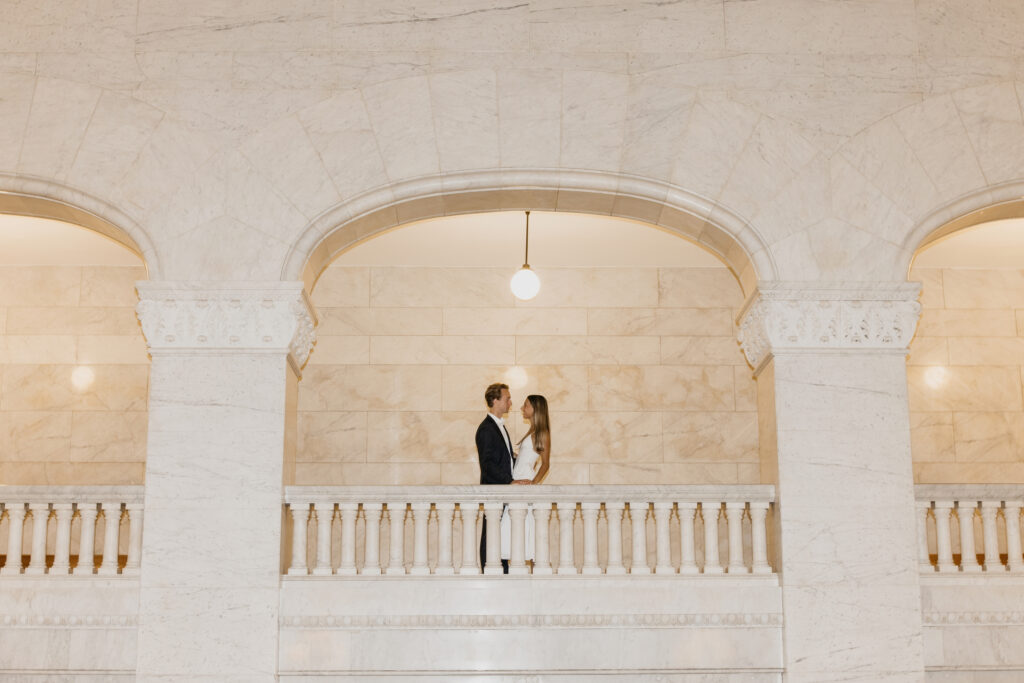 Couple embracing under a marble archway, seen from a distance
