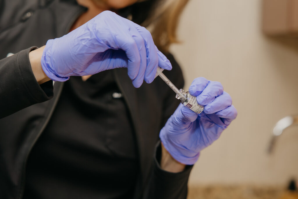 Gloved hands in purple nitrile gloves preparing an injection syringe, med spa treatment room