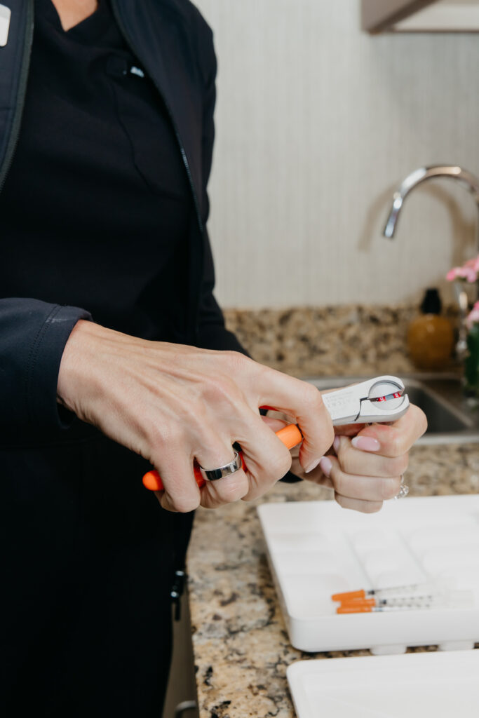 Hands in black scrub sleeves preparing a syringe device at a granite sink counter