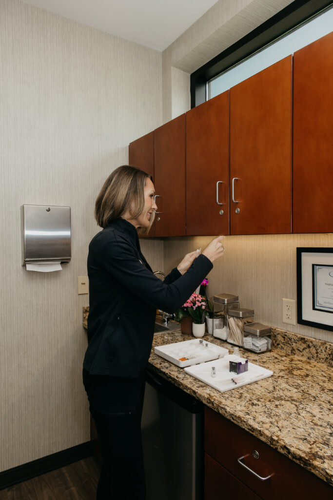 Stephanie Astor standing at a counter organizing skincare and product bottles on a shelf