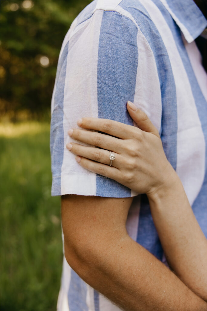 Close-up of woman's hand with engagement ring resting on man's arm in blue striped shirt