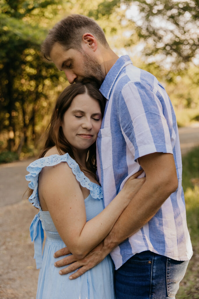 Man kissing woman's forehead on a path, woman in blue dress with eyes closed