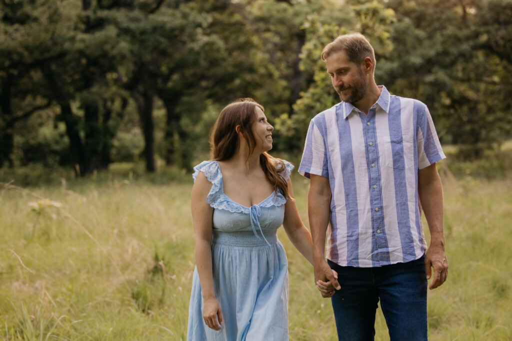 Couple smiling at each other while holding hands in a grassy field
